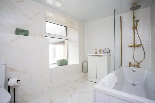 A bathroom with a bathtub, a shower, a window, and a toilet.