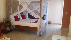 A bedroom with a four-poster bed, a bedside table with a lamp, and a small table with glasses and a bottle.