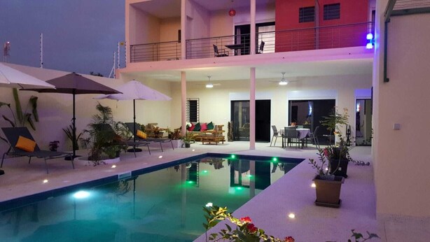 A multi-level indoor pool area with lounge chairs, umbrellas, and potted plants.
