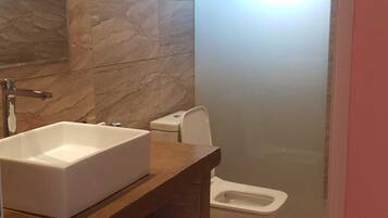 Une salle de bain avec un mur en marbre, un lavabo blanc, des toilettes et un espace douche.