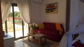 A living room with a red sofa, a wooden coffee table with a vase of flowers, and a painting of a bus on the wall.