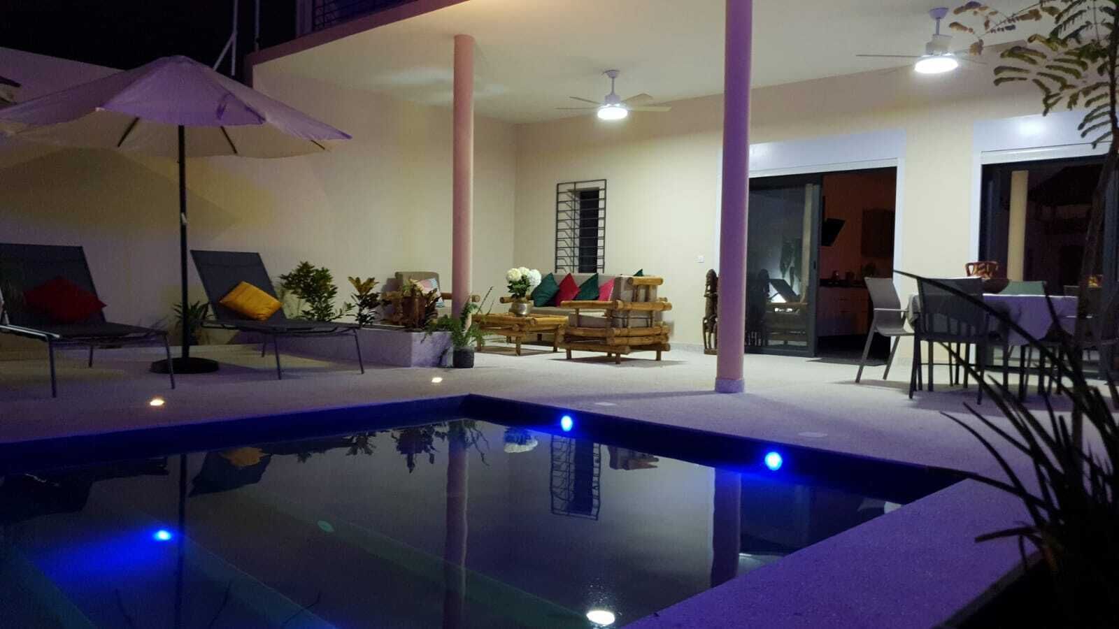 An indoor swimming pool with a lounge area, including chairs and tables, and a ceiling fan.