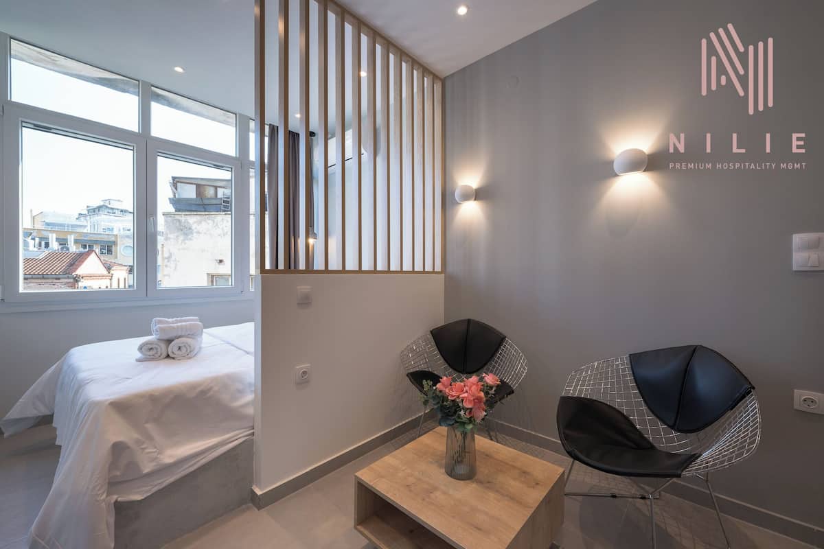 Moderni hotellihuone, jossa on sänky, pieni puinen pöytä, tuoli ja koristeellinen maljakko.
