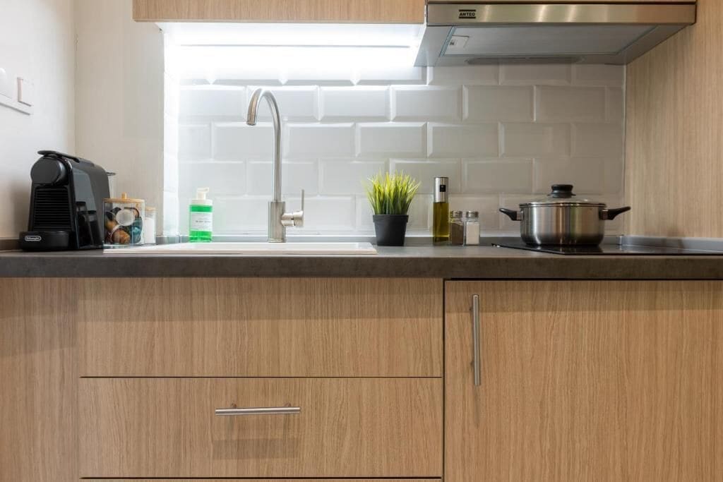 A modern kitchen with wooden cabinets, a stainless steel range hood, a sink with a modern faucet, and a countertop with a coffee maker, a plant, and a pot.