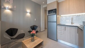 Una cocina moderna con un refrigerador de acero inoxidable, armarios de madera y un lavamanos integrado. Hay dos sillas negras y una mesa de madera con un florero.