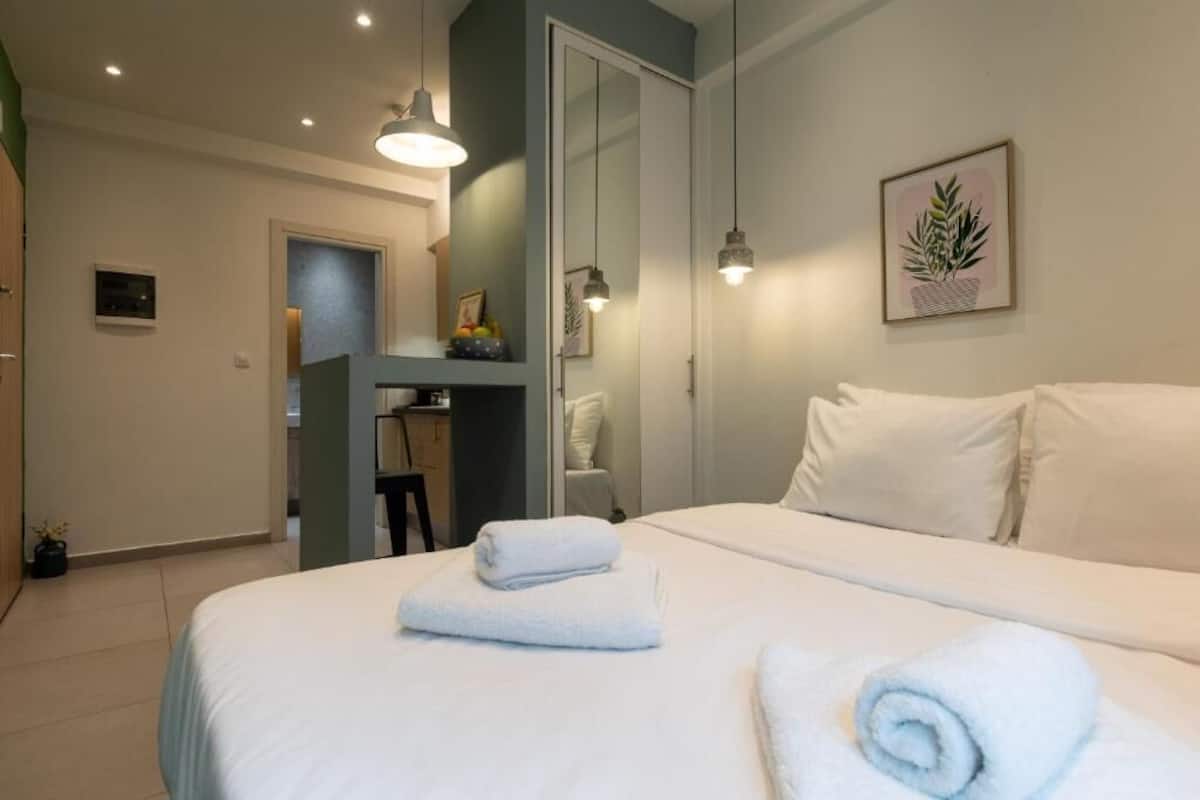 Hotellihuone, jossa on sänky, kaksi yöpöytää, peili ja seinälle kiinnitetty kasvi.
