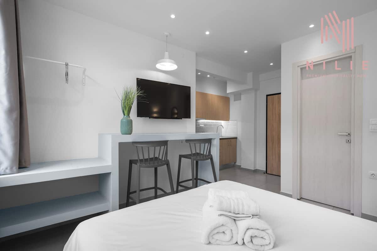 Moderni hotellihuone, jossa on sänky, televisio, pieni keittonurkkaus ja kylpyhuone.