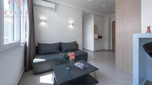Una sala de estar moderna con un sofá gris, una mesa de centro con un jarrón y una revista, y un ventanal con cortinas.