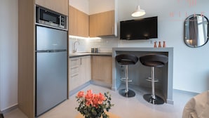 Una cocina moderna con electrodomésticos de acero inoxidable, armarios de madera y un televisor de pantalla plana. Hay dos taburetes de bar y un florero sobre el suelo.