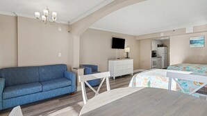 A room with a blue sofa, a dining table, a white dresser, a flat-screen TV, and a kitchen area. - Beautiful, Quiet, Peaceful Studio (Myrtle Beach)