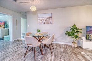Un coin repas avec une table en verre et quatre chaises, une plante en pot et un tableau accroché au mur.
