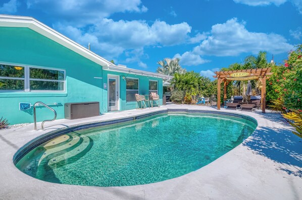 Une maison turquoise avec une piscine, du mobilier d’extérieur et une pergola.
