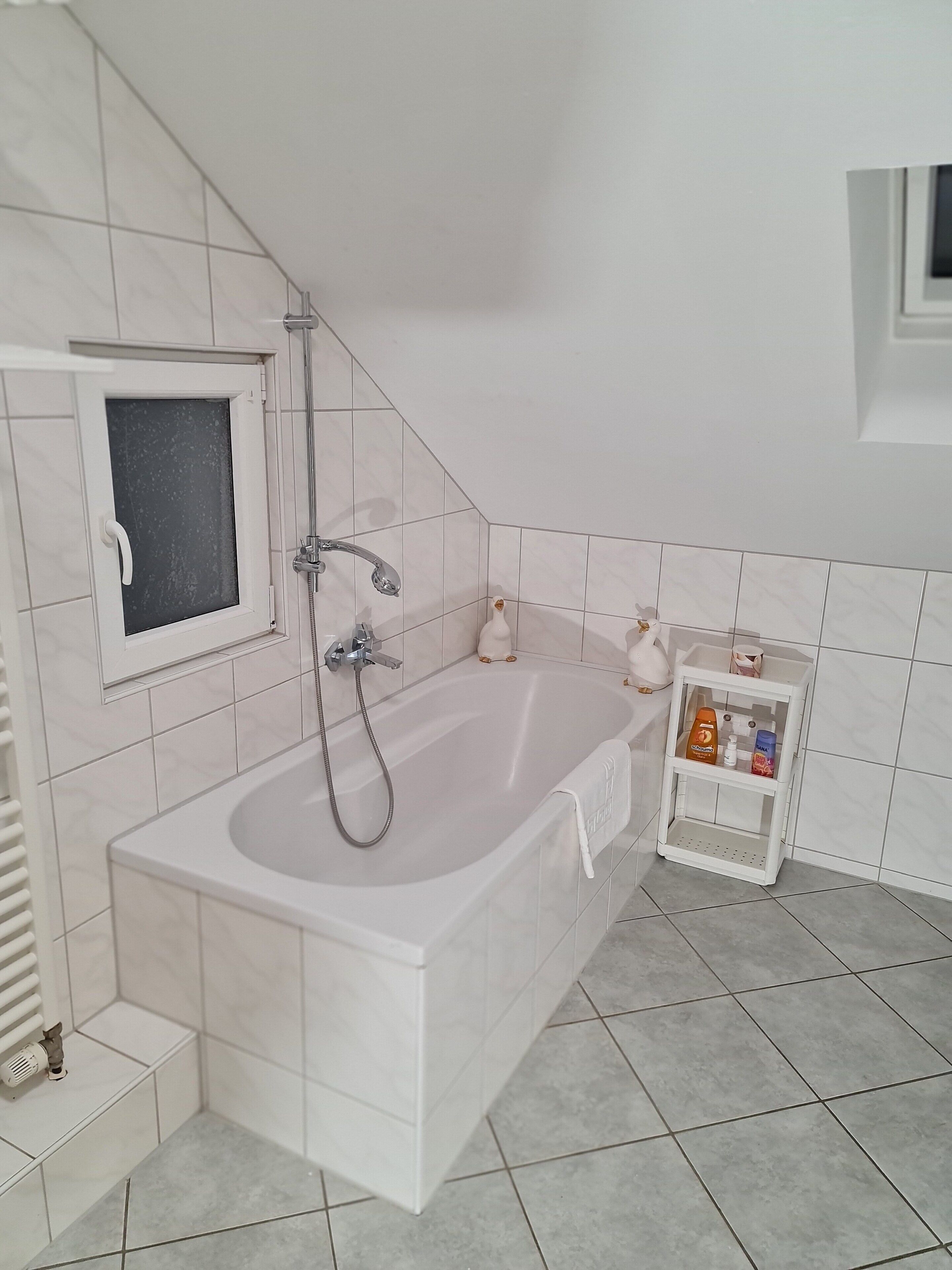 Et badeværelse med badekar, bruser og en lille hylde med toiletartikler.