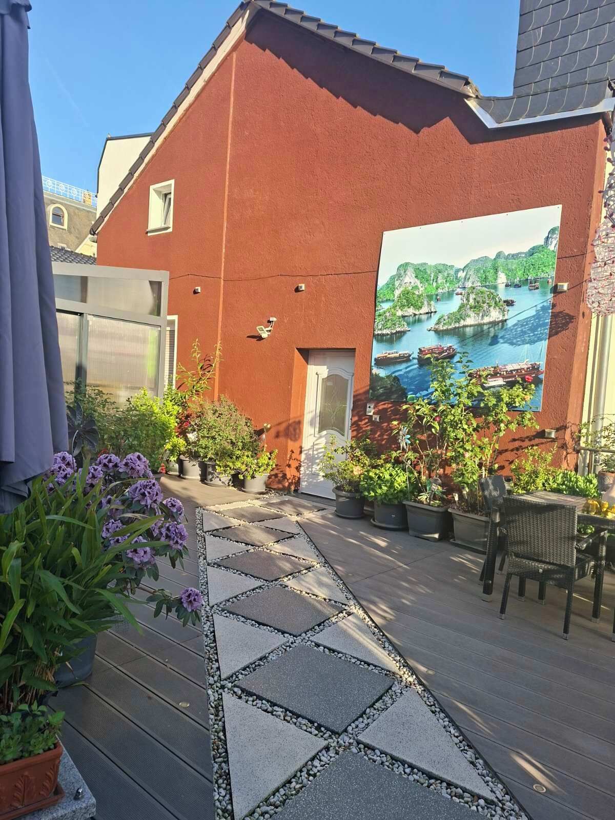 En innergård med en röd byggnad, utomhusmöbler och en väggmålning som föreställer ett kustlandskap.