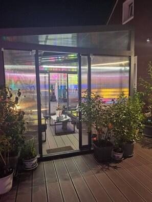 An outdoor patio area with a glass door entrance, potted plants, and a seating area with tables and chairs. - City apartment with sleeping gallery for up to 6 guests directly in the city center of Neuwied (Neuwied)