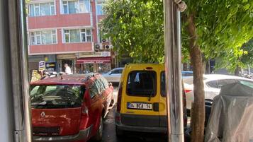 Un'area di parcheggio con un'auto rossa e un furgone giallo, un albero e un edificio con segnaletica sullo sfondo.