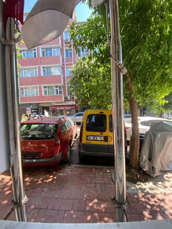 A parking area with a red car and a yellow van, a tree, and a building with signage in the background.