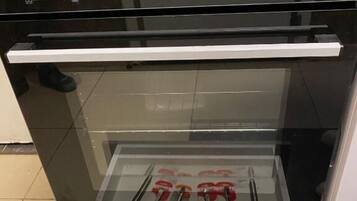 An open oven with a drawer below containing neatly arranged cutlery sets.