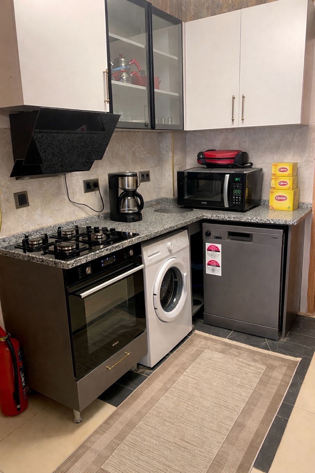 A compact kitchen with a gas stove, a microwave, a washing machine, and a dishwasher.