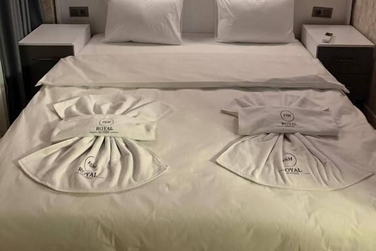 A hotel room with a large bed, two bedside tables, and a wooden textured wall.