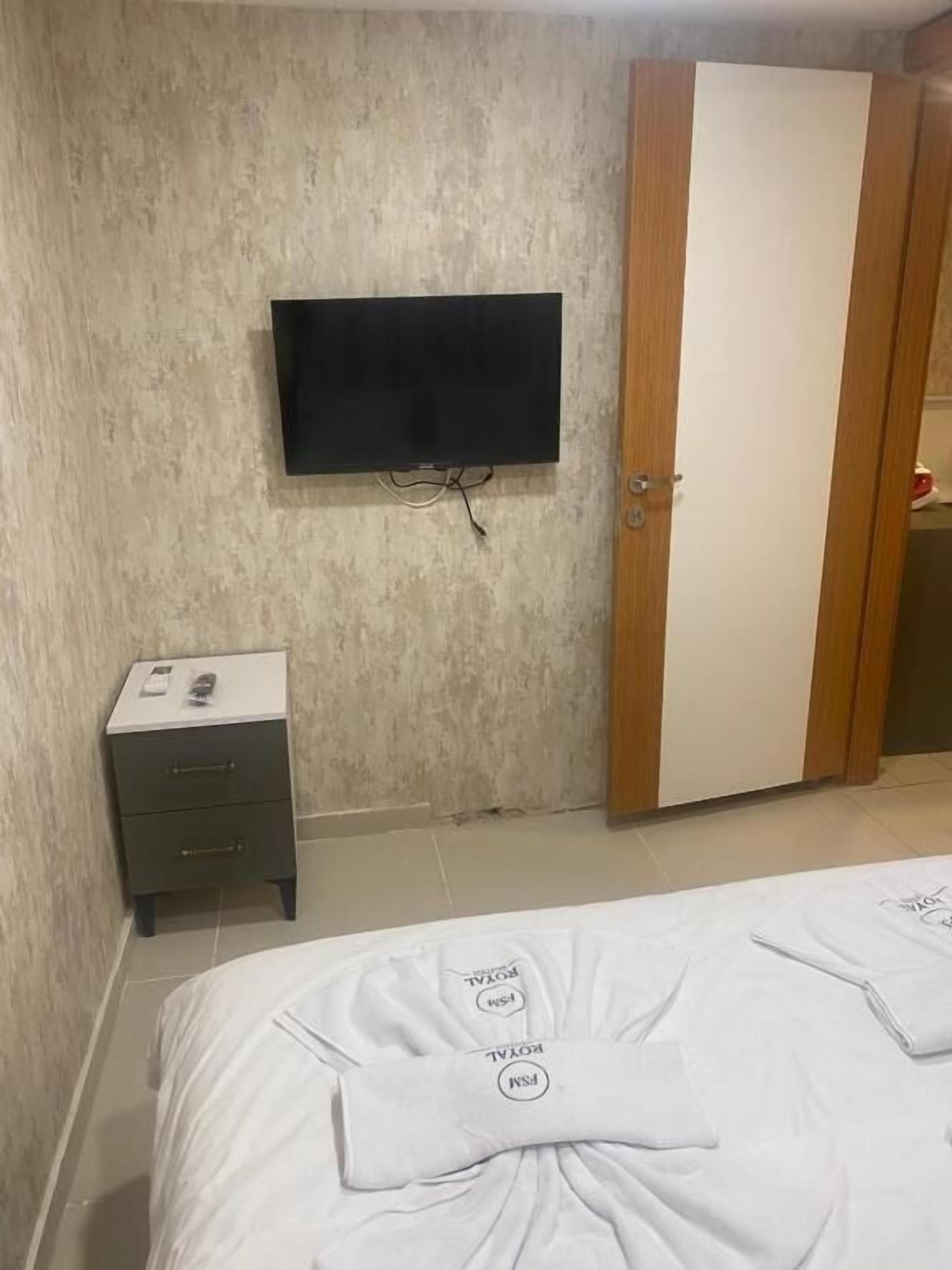 A bedroom with a bed, a TV mounted on the wall, a bedside table, and a wardrobe.