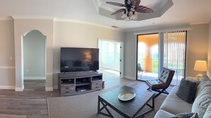 Ein Wohnzimmer mit Flachbildfernseher, einer Couch, einem Couchtisch und einem Deckenventilator.
