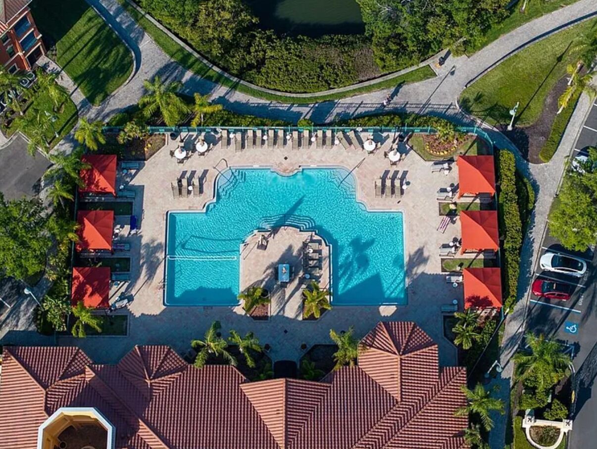 Luchtbeeld van een resort met een centraal zwembad, meerdere loungegedeeltes en een parkeerplaats.