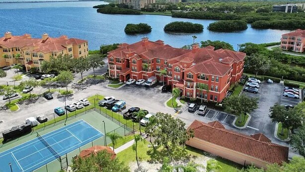 Ein Hotelkomplex mit mehreren Gebäuden mit roten Dächern, einem Tennisplatz und einem Yachthafen mit Booten.