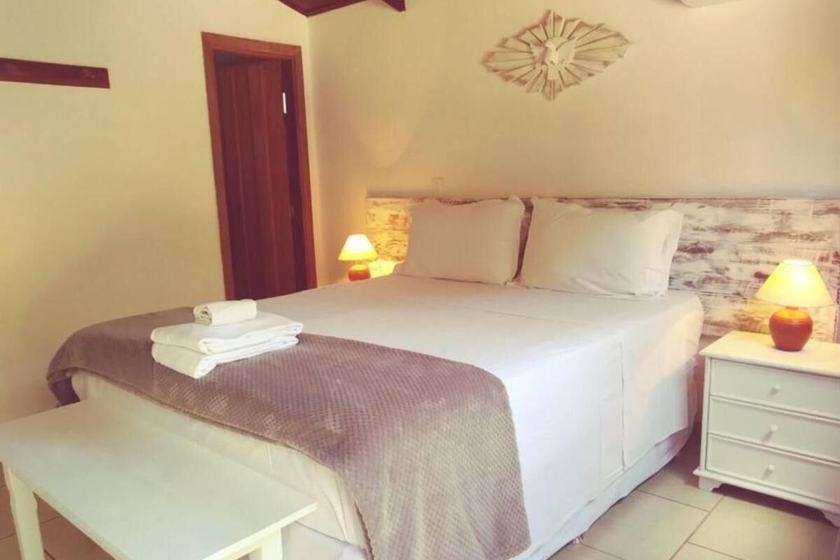 A neatly made bed with a white and brown blanket, a bedside table with a lamp, and a wall-mounted air conditioner.