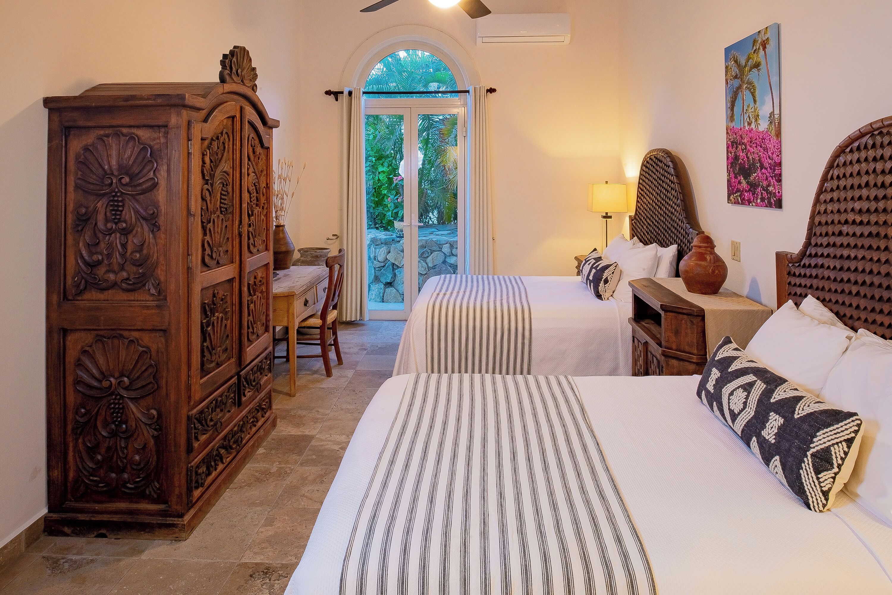 Une chambre d’hôtel avec deux lits, une armoire en bois, une petite table et une vue sur l’extérieur grâce à une porte vitrée.