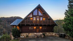 Una baita di legno con fondamenta in pietra, ampie finestre e un balcone.