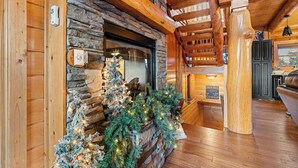 Interno di una baita con camino in pietra, travi in legno e albero di Natale.
