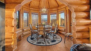 Interno di una baita di legno con zona pranzo, ampie finestre e un lampadario.