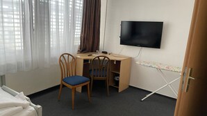 A room with a bed, a desk with a chair, a television, and a window with curtains. - Hotel RI (Esslingen)