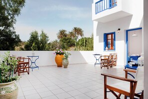 A terrace with white tiled flooring, wooden furniture, and potted plants. - HOTEL ELENI (Milos)