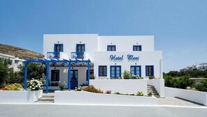 A white building with a blue facade, a sign reading "Hotel Eleni," and a covered entrance with blue railings. - HOTEL ELENI (Milos)