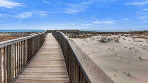 Ein Holzsteg führt zu einem Strand unter blauem Himmel.