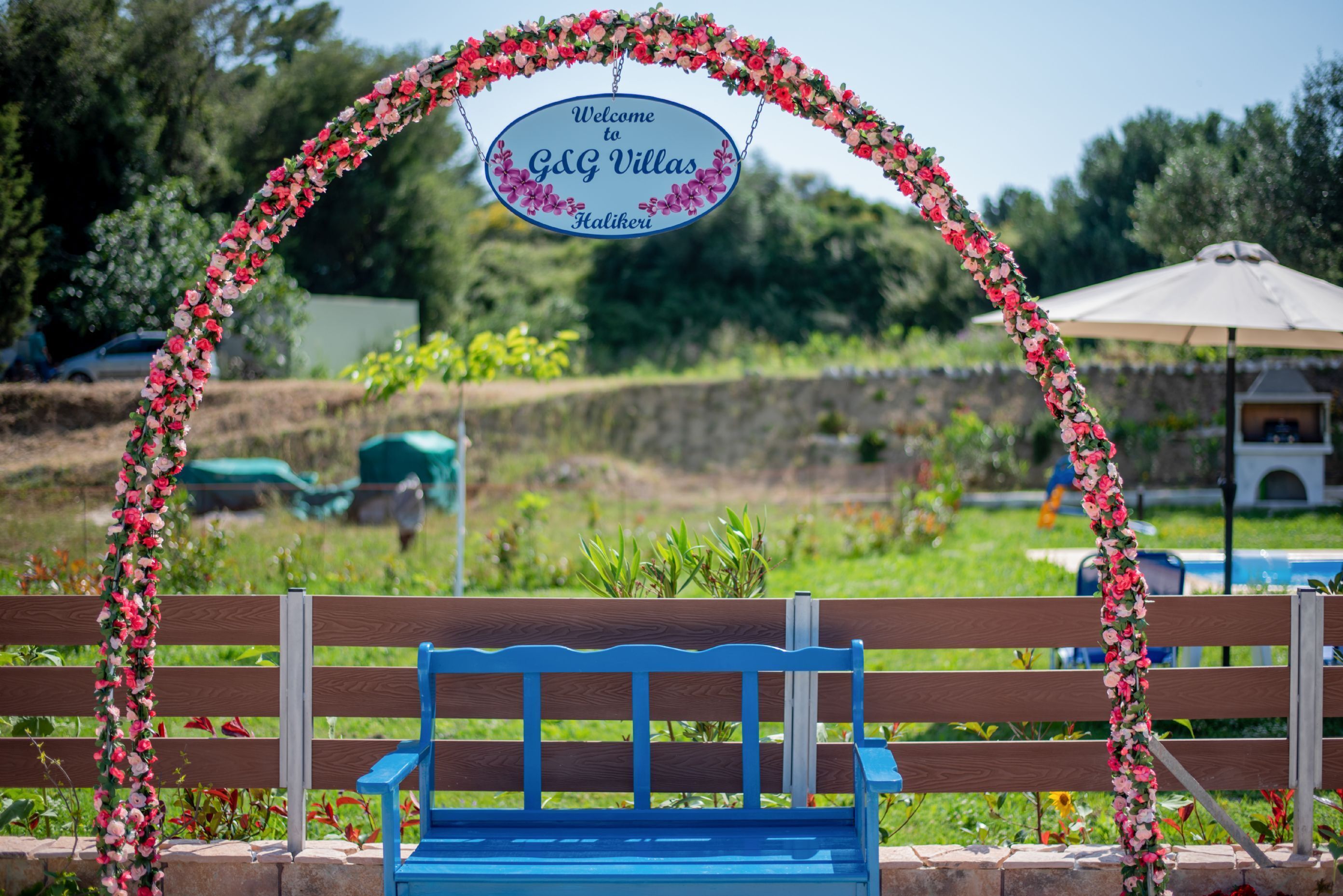 Een bank met een bloemrijke bogenpoort en een bordje met daarop 'Welcome to G&G Villas Halikeri'.
