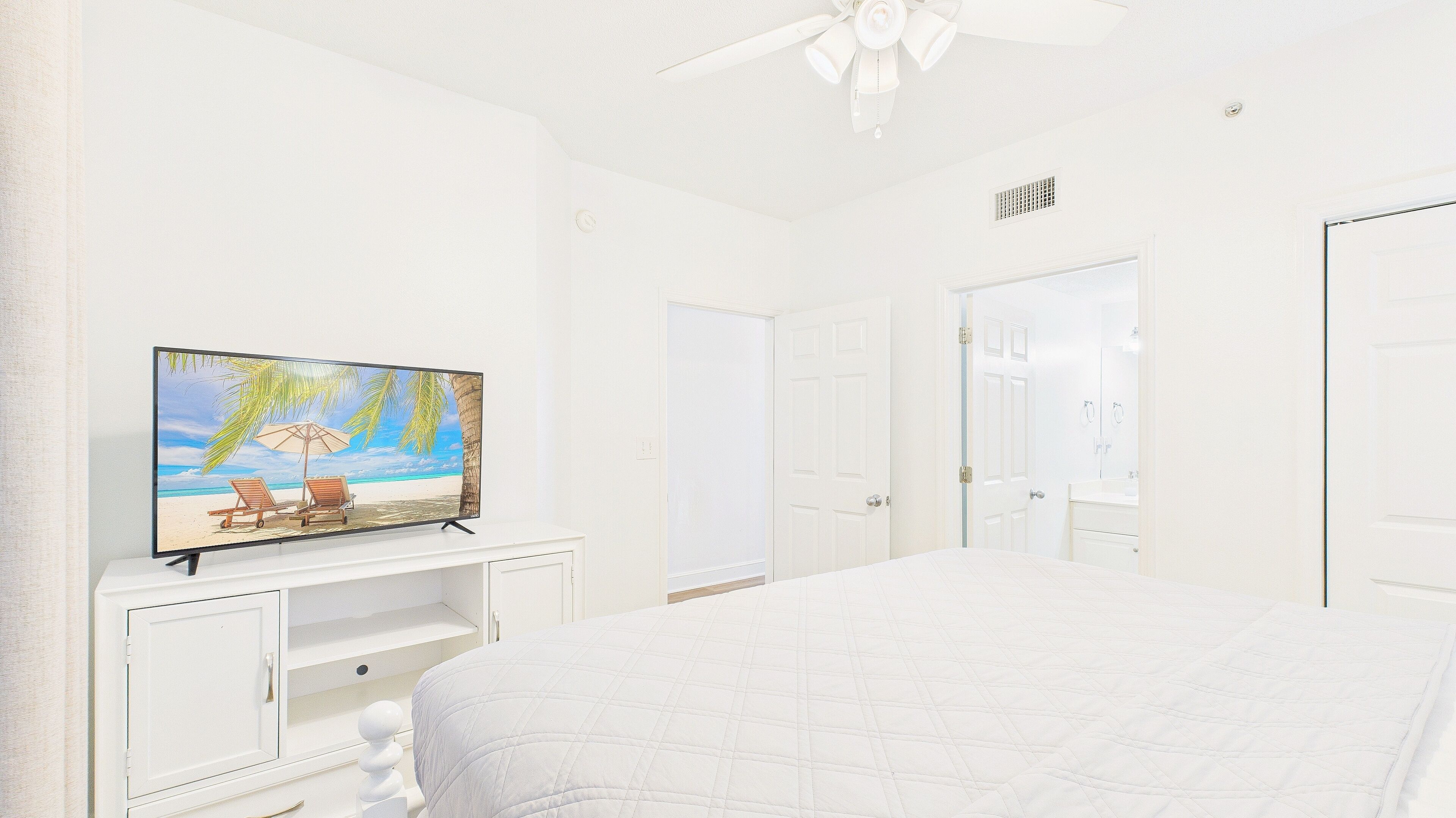 A bedroom with a bed, a TV on a stand, a ceiling fan, and white doors.