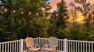 Eine Terrasse mit zwei Korbstühlen und einer Lichterkette vor Bäumen und einem Sonnenuntergang.