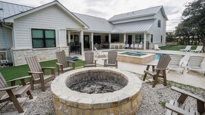 Ein überdachter Außenbereich mit Feuerstelle, Liegestühlen und Pool.
