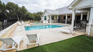 Ein Garten mit Schwimmbad, weißen Liegestühlen und einer überdachten Terrasse.