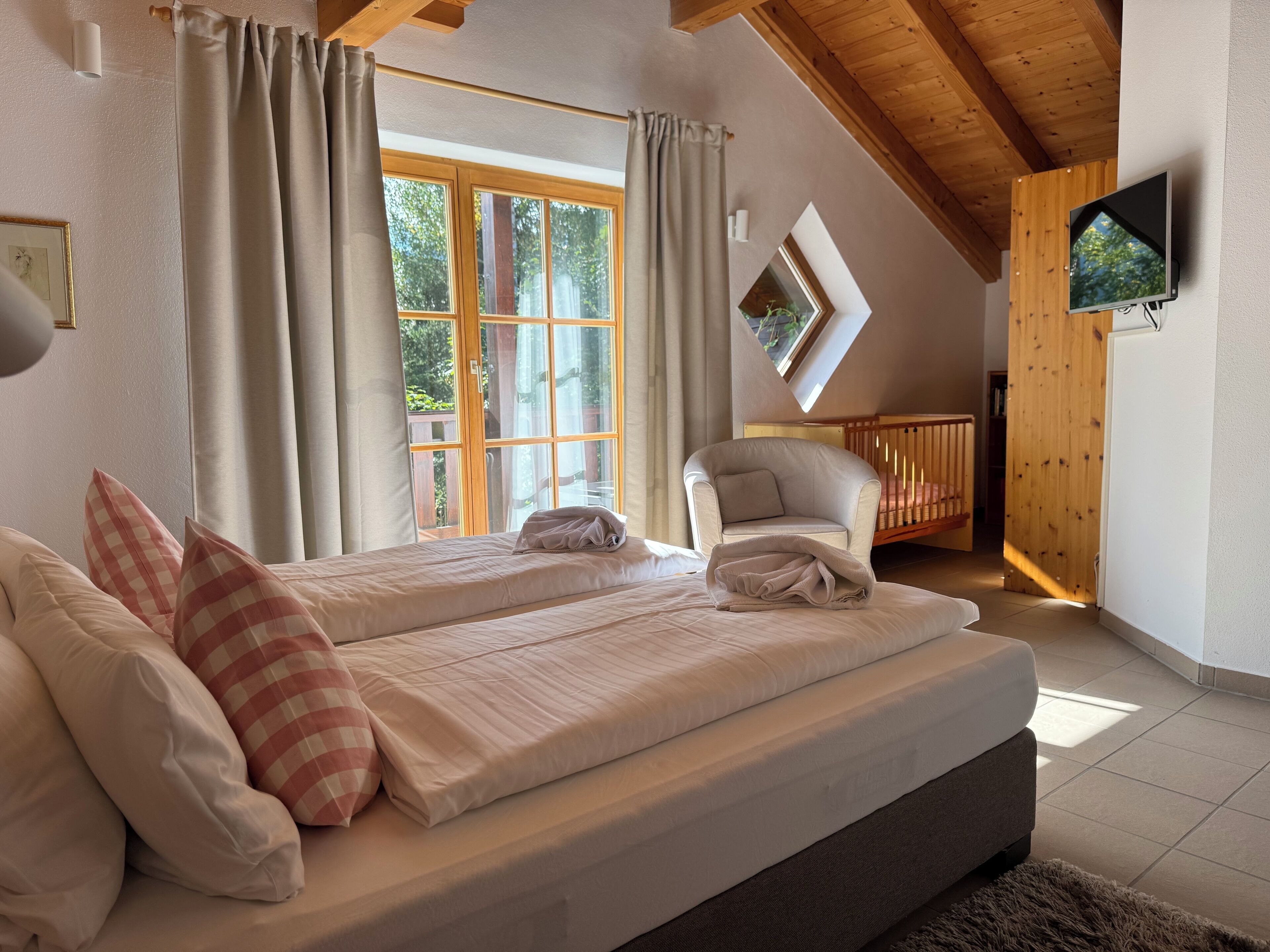 Ein Schlafzimmer mit zwei Betten, Holzboden, Fernseher und einem Fenster mit Vorhängen.