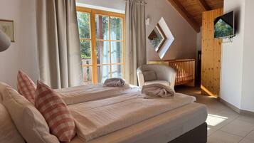 Ein Schlafzimmer mit zwei Betten, Holzboden, Fernseher und einem Fenster mit Vorhängen.