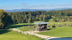 Een golfbaan met een clubhuis, een vijver en bebossing op de achtergrond.