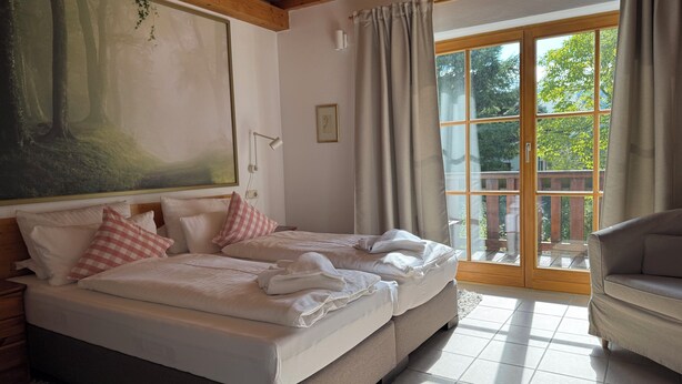 Een slaapkamer met een groot bed, een slaapbank, een schilderij en een schuifdeur naar buiten.
