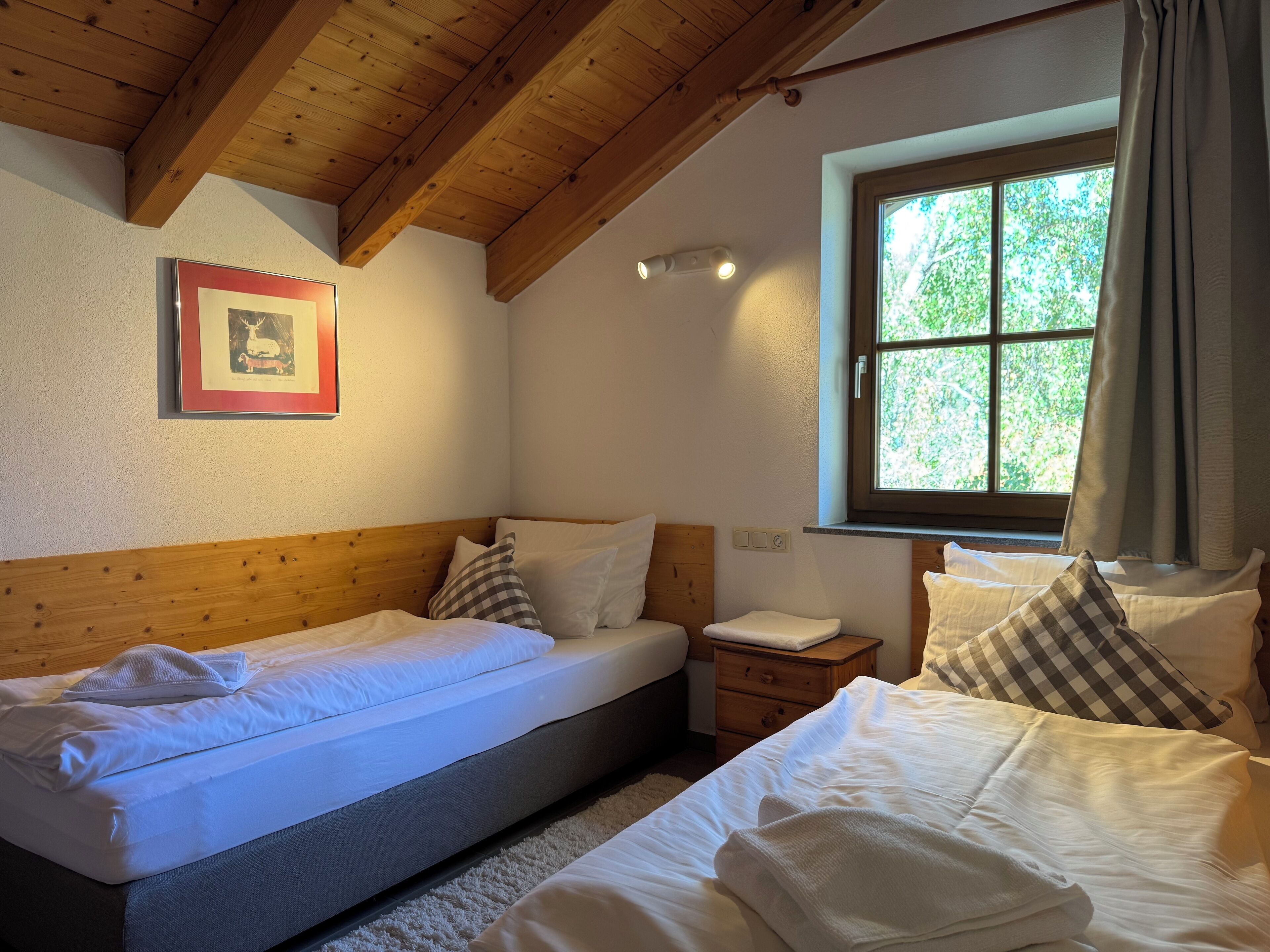 Quarto com duas camas, teto de madeira, janela com cortinas e um quadro na parede.