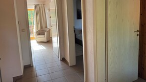 Een gang met een deur naar een slaapkamer, een stoel en een bed.