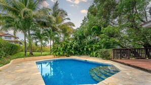 Una piscina con baldosas de piedra, rodeada de abundante vegetación y palmeras.