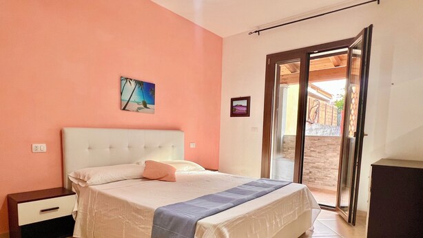 Ein Schlafzimmer mit einem Bett, einem Nachttisch, einer Tür zu einem Außenbereich und einem Wandbild.